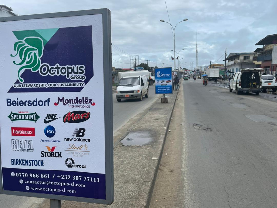 An Octopus Group roadside billboard displaying consumer brands beside a busy street in Freetown